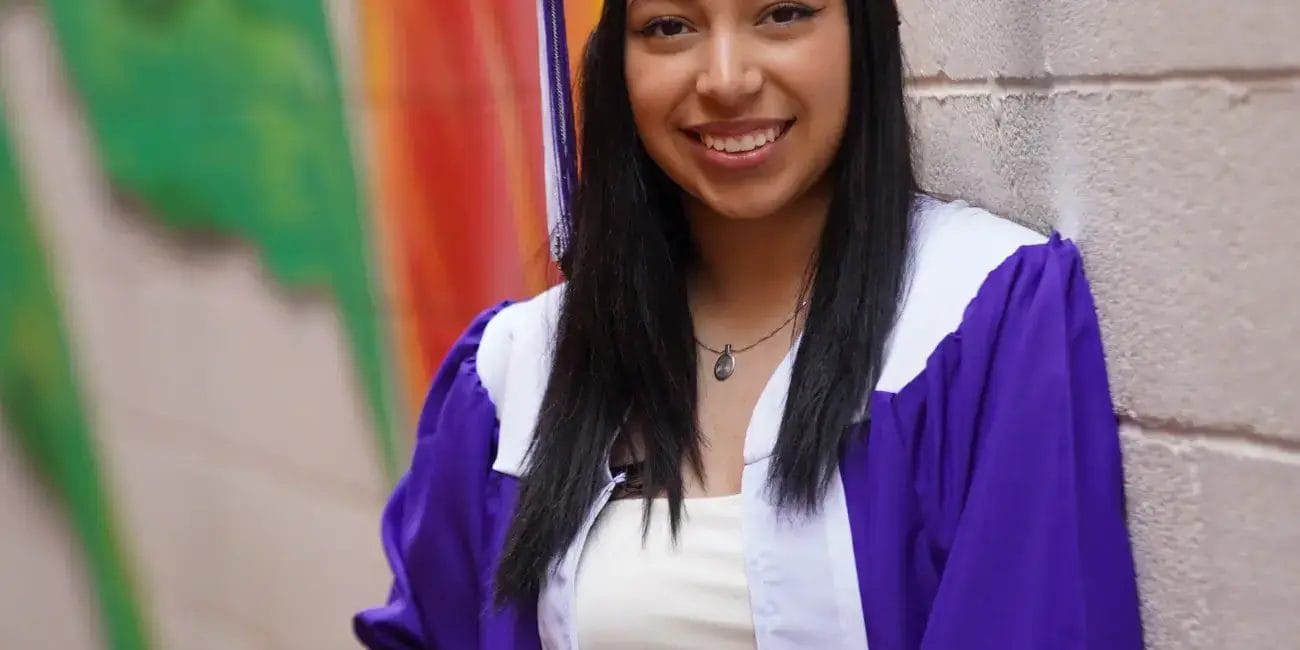 A woman wearing a blue graduation gown, smiling proudly at her graduation ceremony.