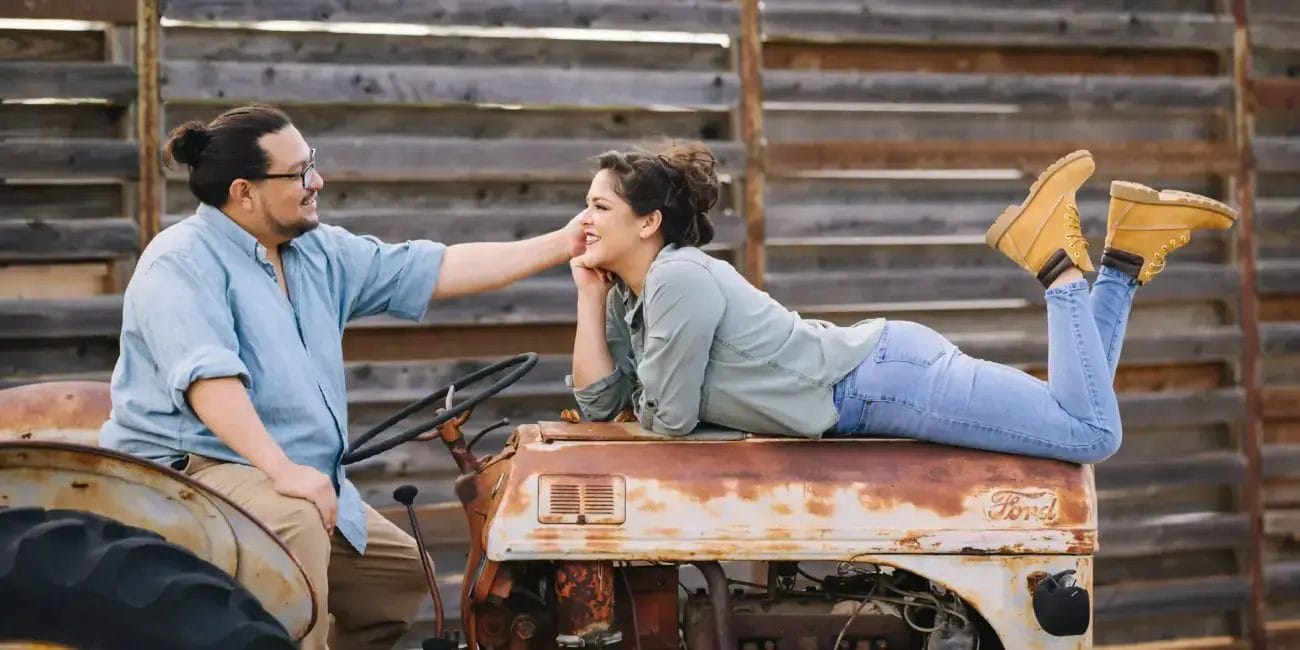 Danny and Rachel pose on an old tractor, enjoying a photo shoot together in a rustic setting.