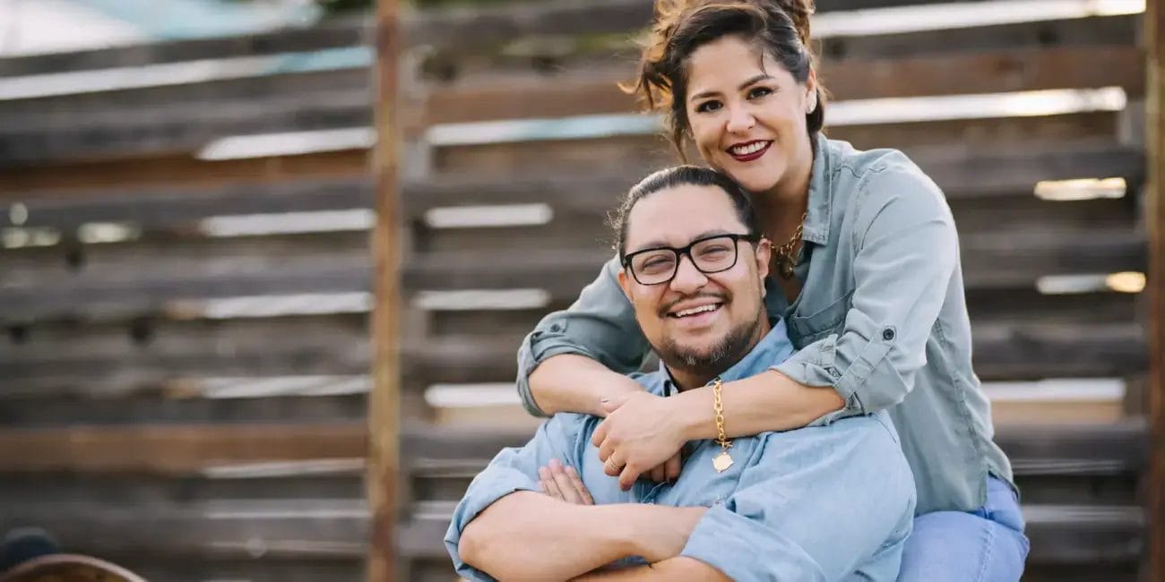 A photo shoot featuring Danny and Rachel, a man and woman, sitting side by side on a bench, both smiling.