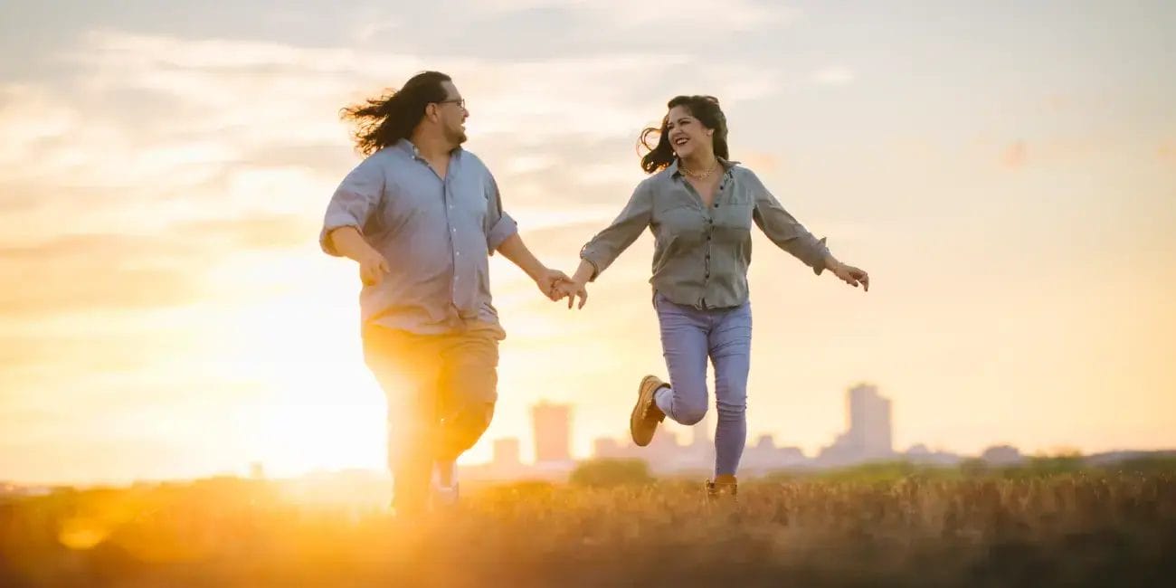 Danny and Rachel run joyfully through a sunlit field at sunset, capturing a moment of happiness and freedom.
