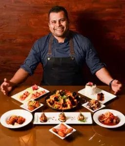 A man seated at a table surrounded by various plates of food, enjoying a meal in a casual dining setting.