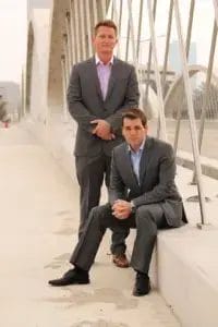 Two men in suits smiling for a photo while standing on a bridge.