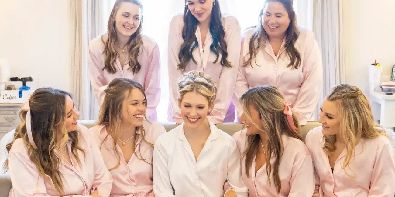 Bride and bridesmaids wearing matching pink robes, smiling together in a joyful pre-wedding moment.