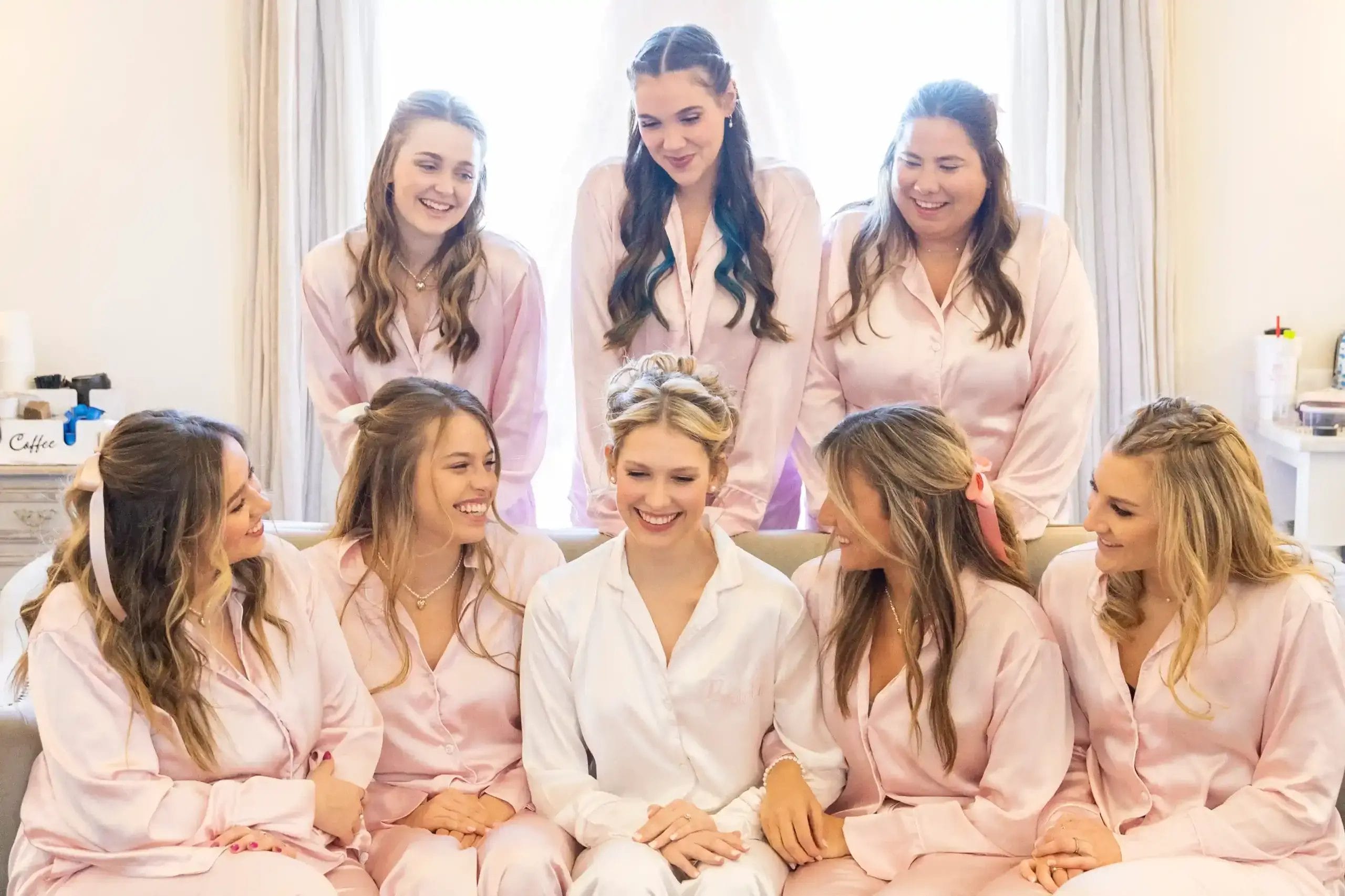 Bride and bridesmaids wearing matching pink robes, smiling together in a joyful pre-wedding moment.