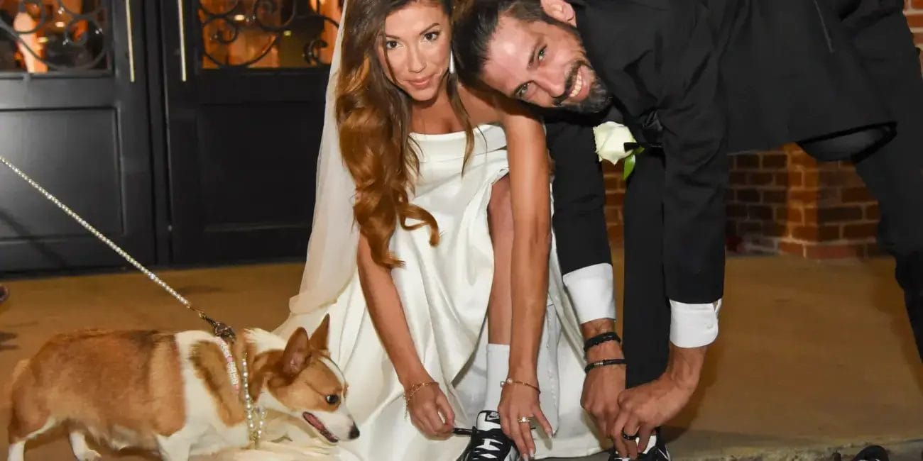 A bride and groom pose with their dog in front of a beautifully decorated wedding venue.