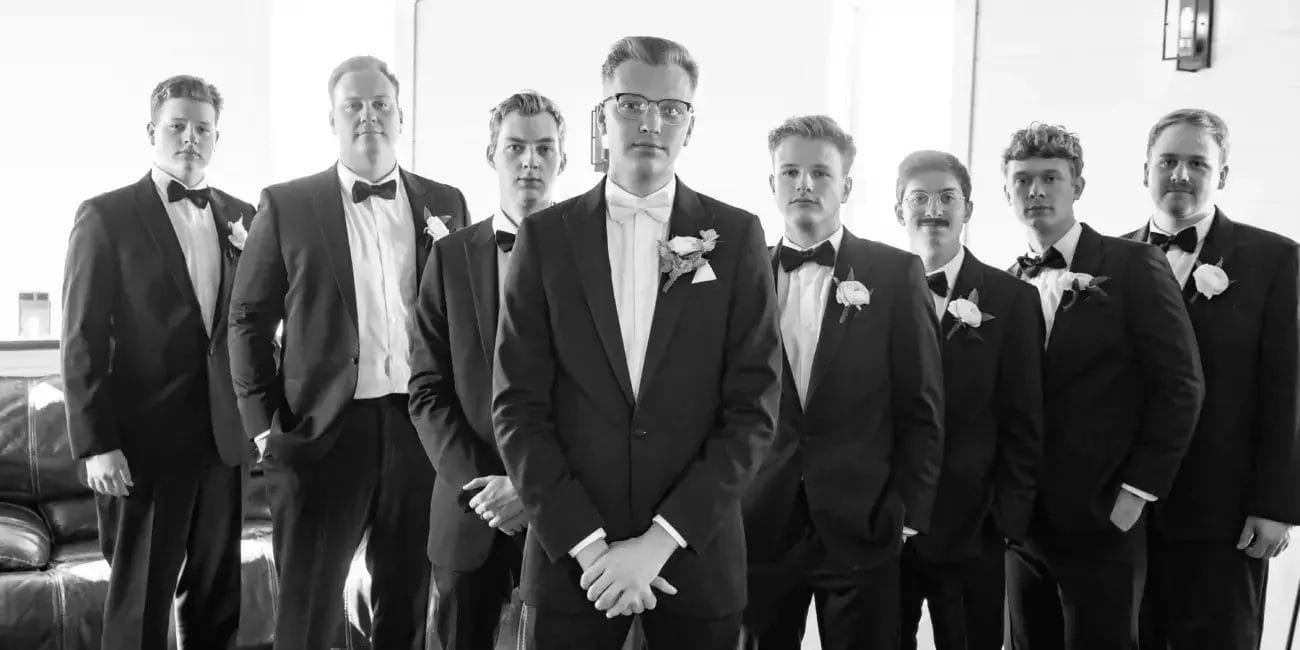 Groom and groomsmen dressed in black and white suits, posing together in a formal setting.