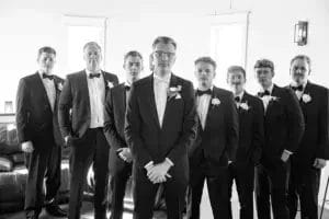 Groom and groomsmen dressed in black and white suits, posing together in a formal setting.