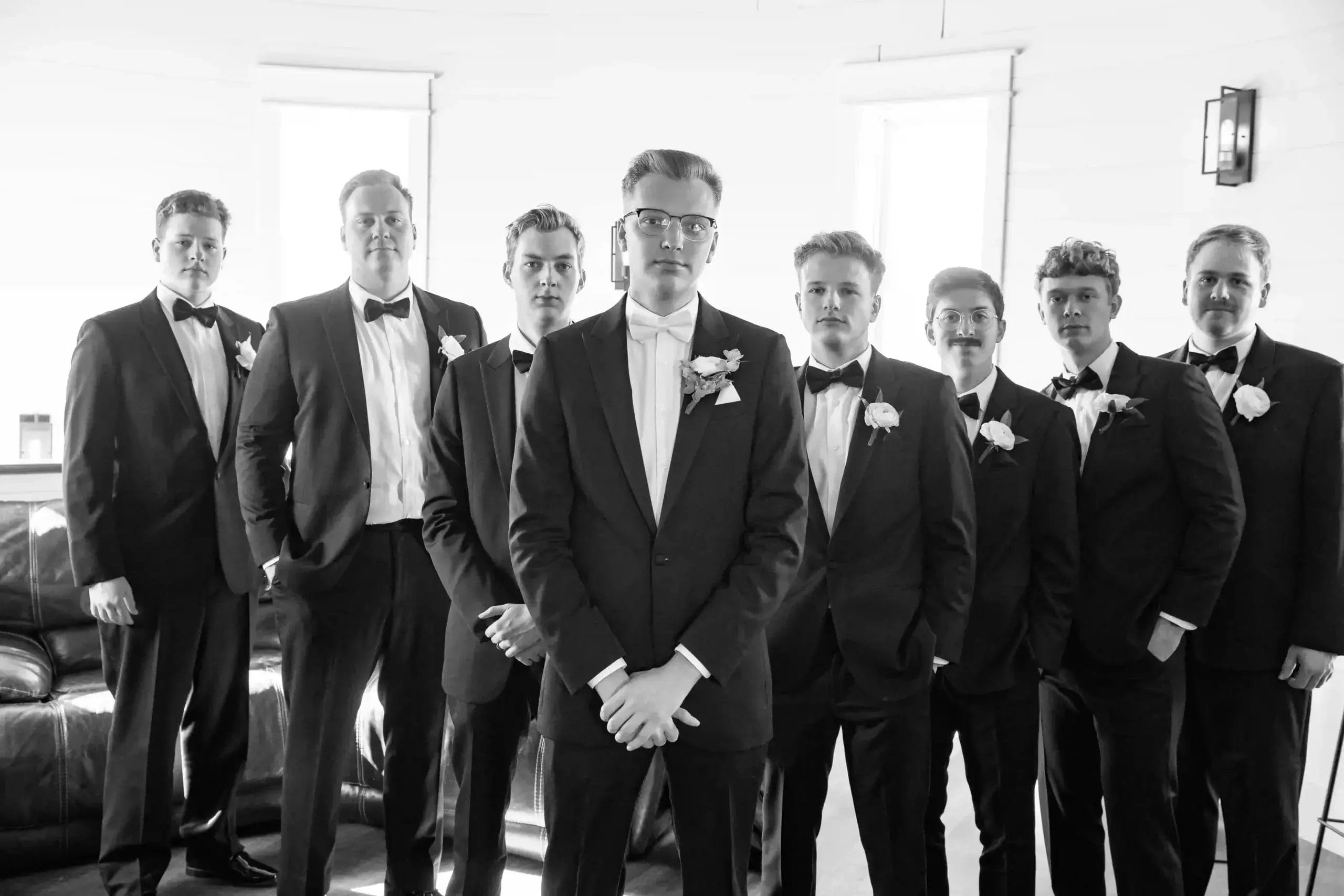 Groom and groomsmen dressed in black and white suits, posing together in a formal setting.