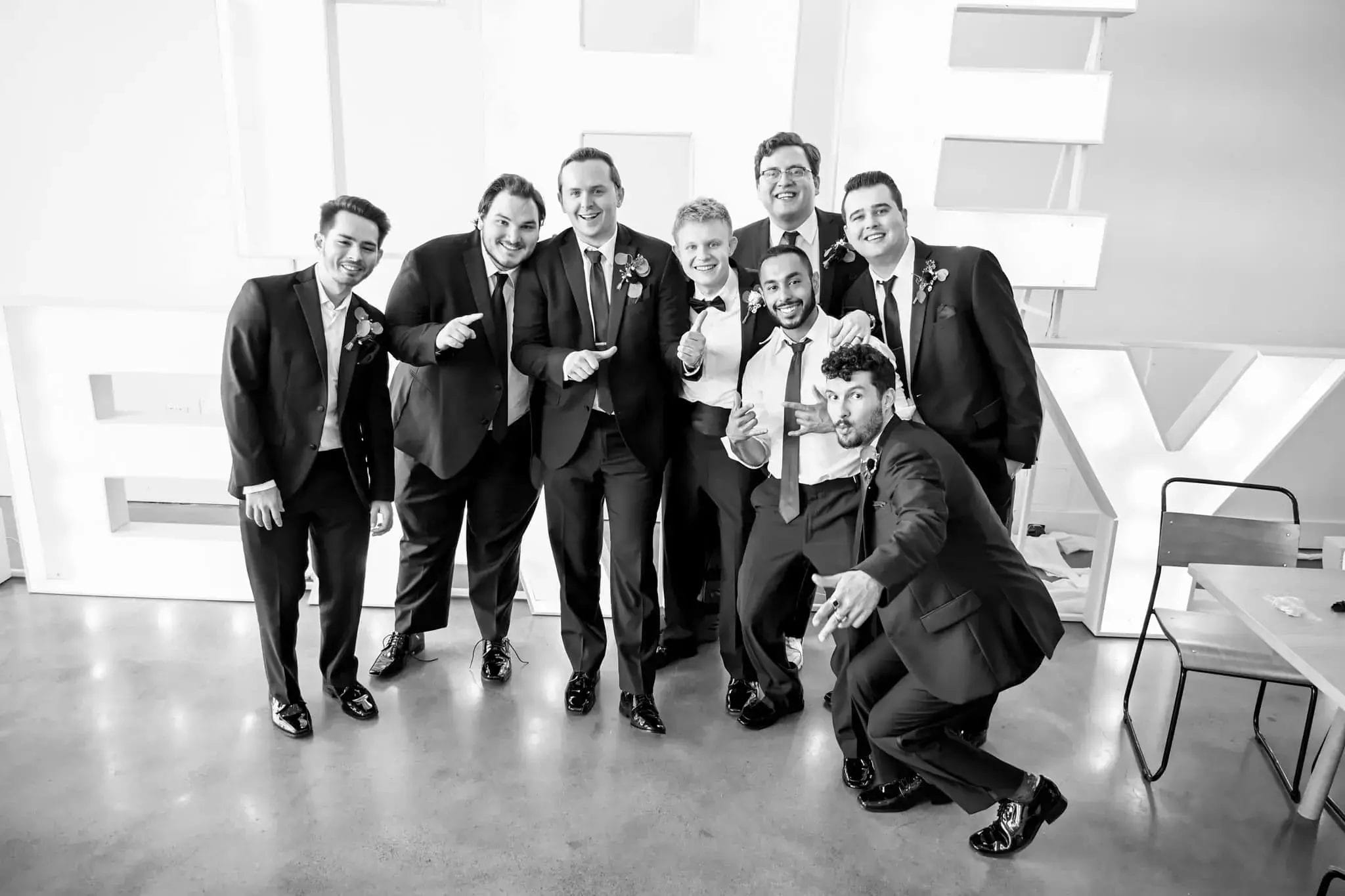 The groom and groomsmen pose together in front of large decorative letters, smiling for the camera.