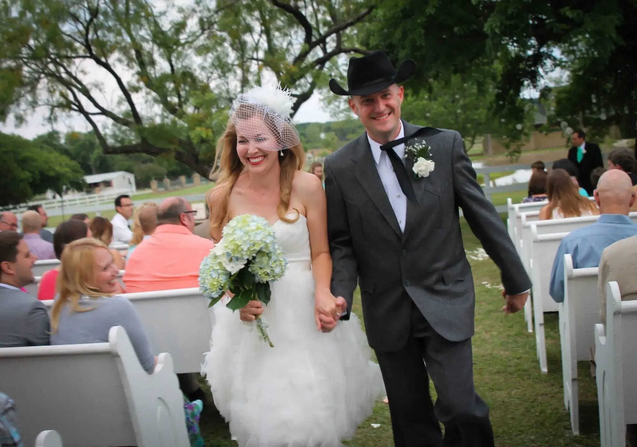 A bride and groom joyfully walk down the aisle, surrounded by floral decorations and smiling guests.