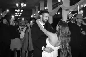 A bride and groom share a romantic dance at their wedding reception, surrounded by joyful guests and festive decorations.