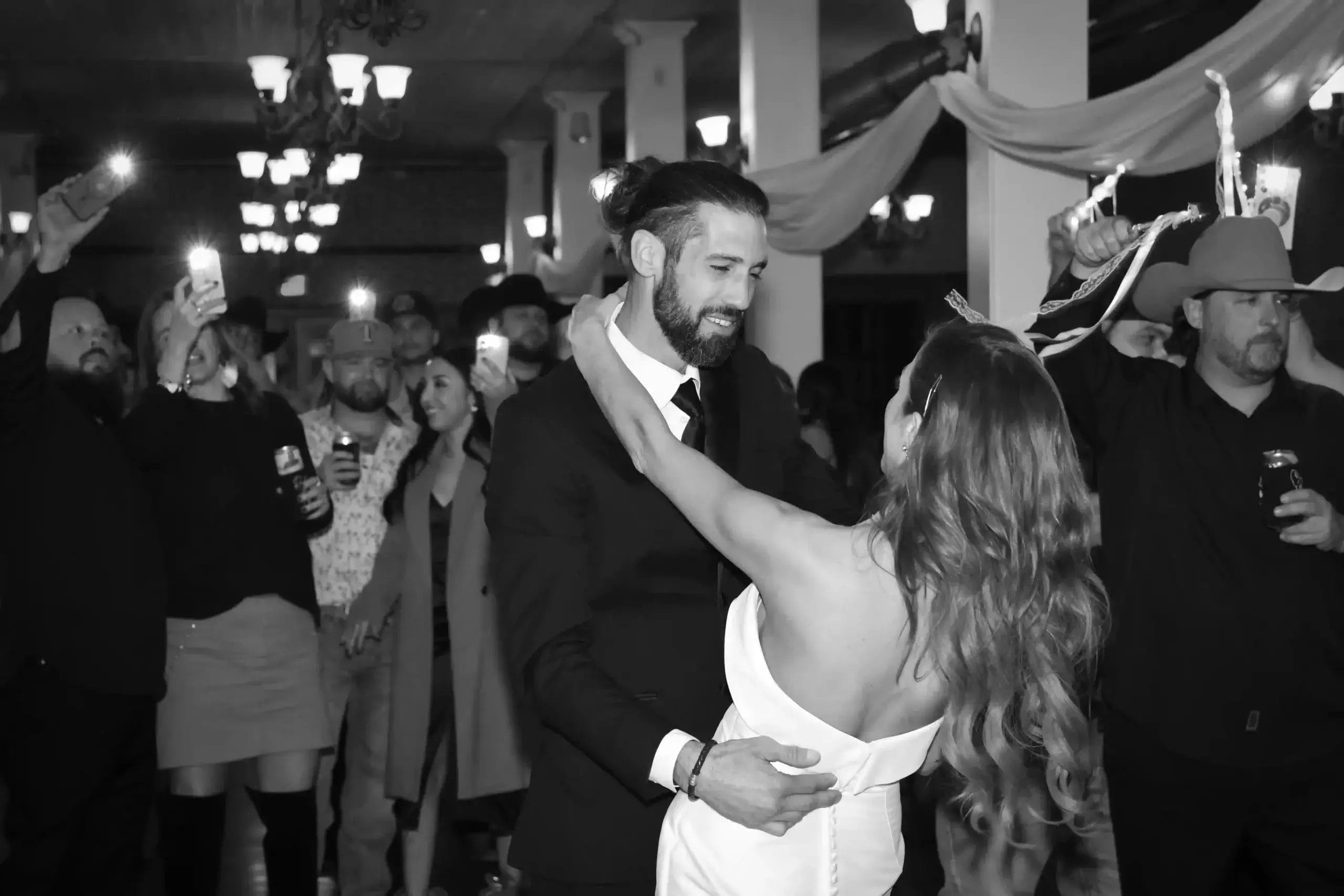 A bride and groom share a romantic dance at their wedding reception, surrounded by joyful guests and festive decorations.