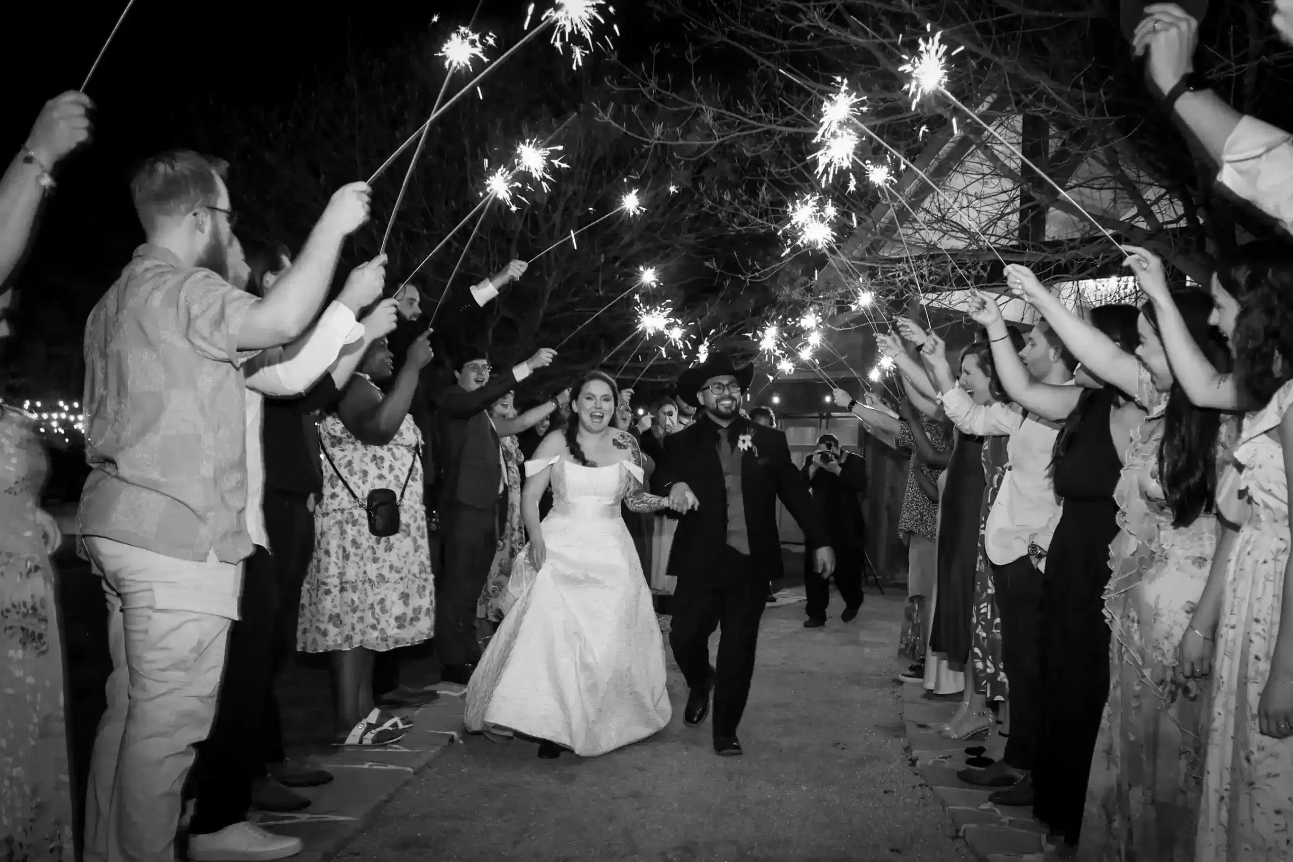 A bride and groom walk down the aisle, surrounded by guests holding sparklers, celebrating their marriage.