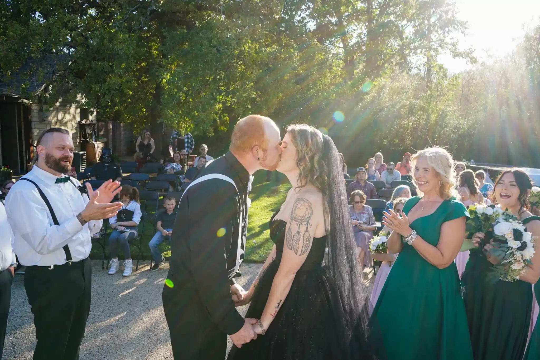 A bride and groom share a kiss during their outdoor wedding ceremony, surrounded by nature and guests celebrating their union.