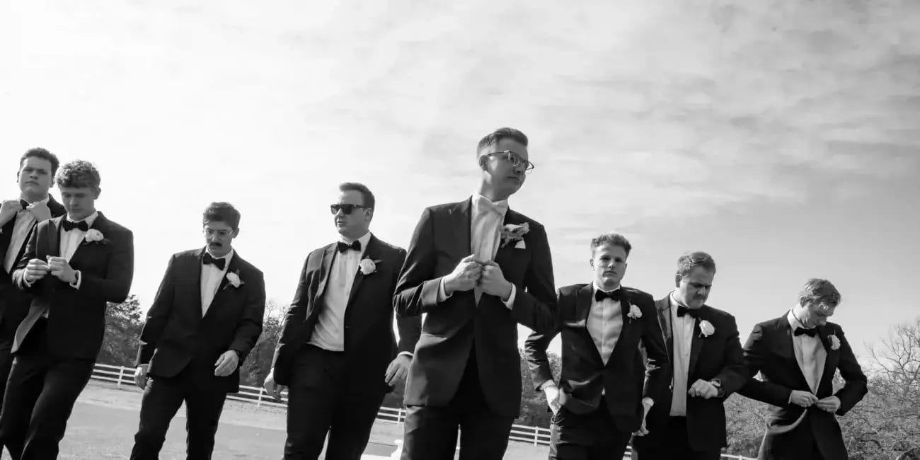 Groomsmen in formal suits walking together across a grassy field, smiling and enjoying the moment.