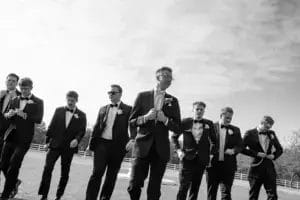 Groomsmen in formal suits walking together across a grassy field, smiling and enjoying the moment.