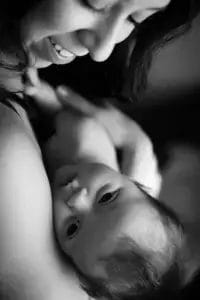 Black and white close-up of a smiling woman cradling a baby. The baby looks up affectionately, resting its head against the woman's arm. Both appear content and connected, highlighting a tender moment.